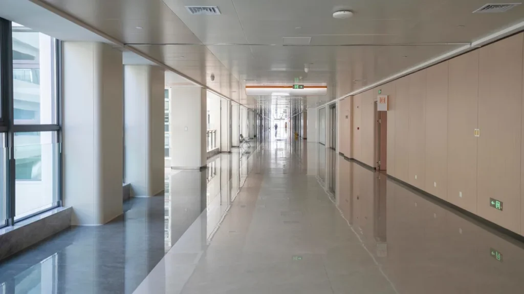 Corredor hospitalar com grandes janelas, luz natural e portas de consultórios.